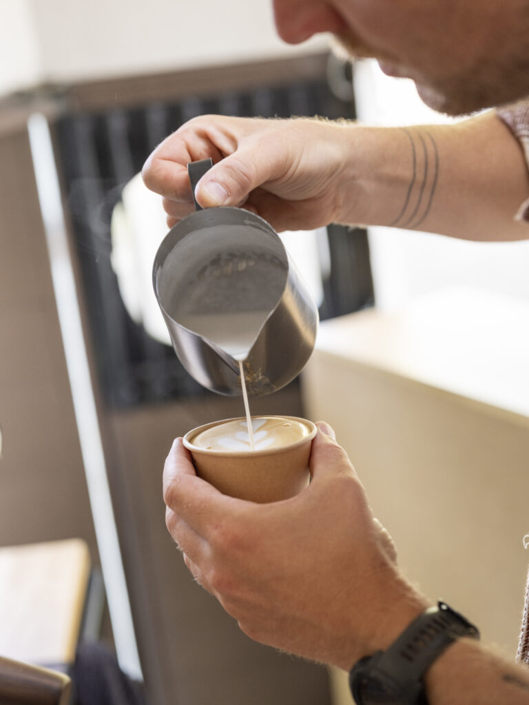 Barista schenkt melk voor latte art in een kop koffie